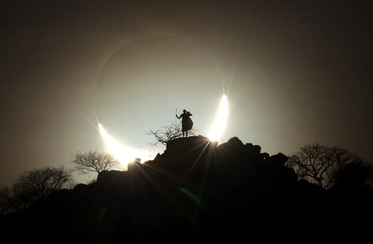 A person on a hilltop silhouetted by a solar eclipse. 